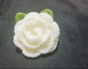 Crocheted white flower with green leaves.