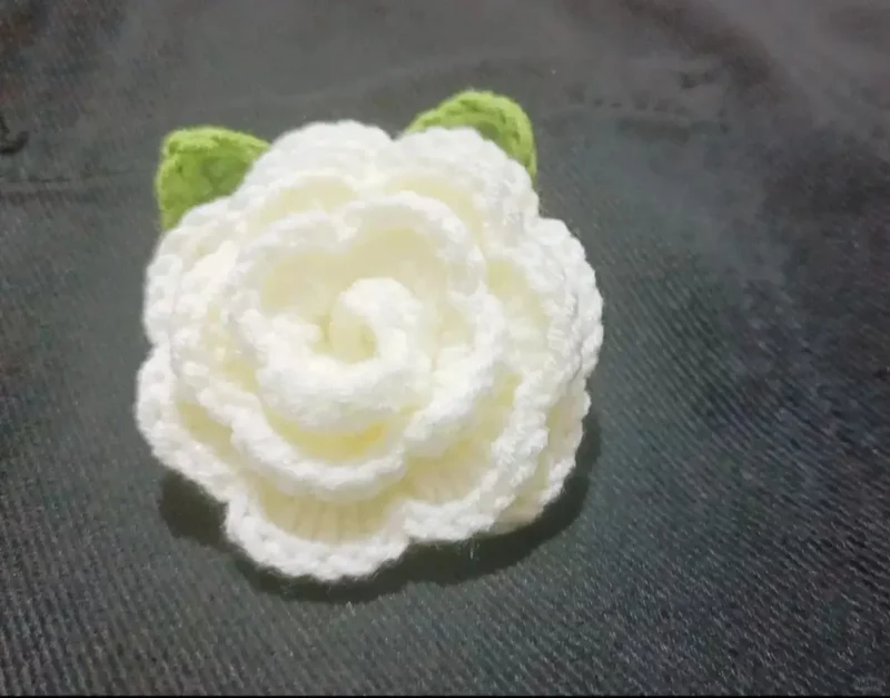 Crocheted white flower with green leaves.