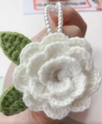 Crocheted white flower with green leaves, pearl necklace.