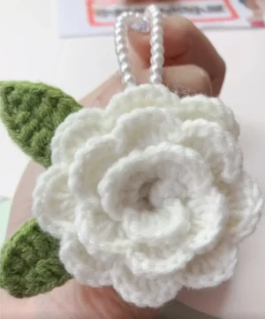 Crocheted white flower with green leaves, pearl necklace.