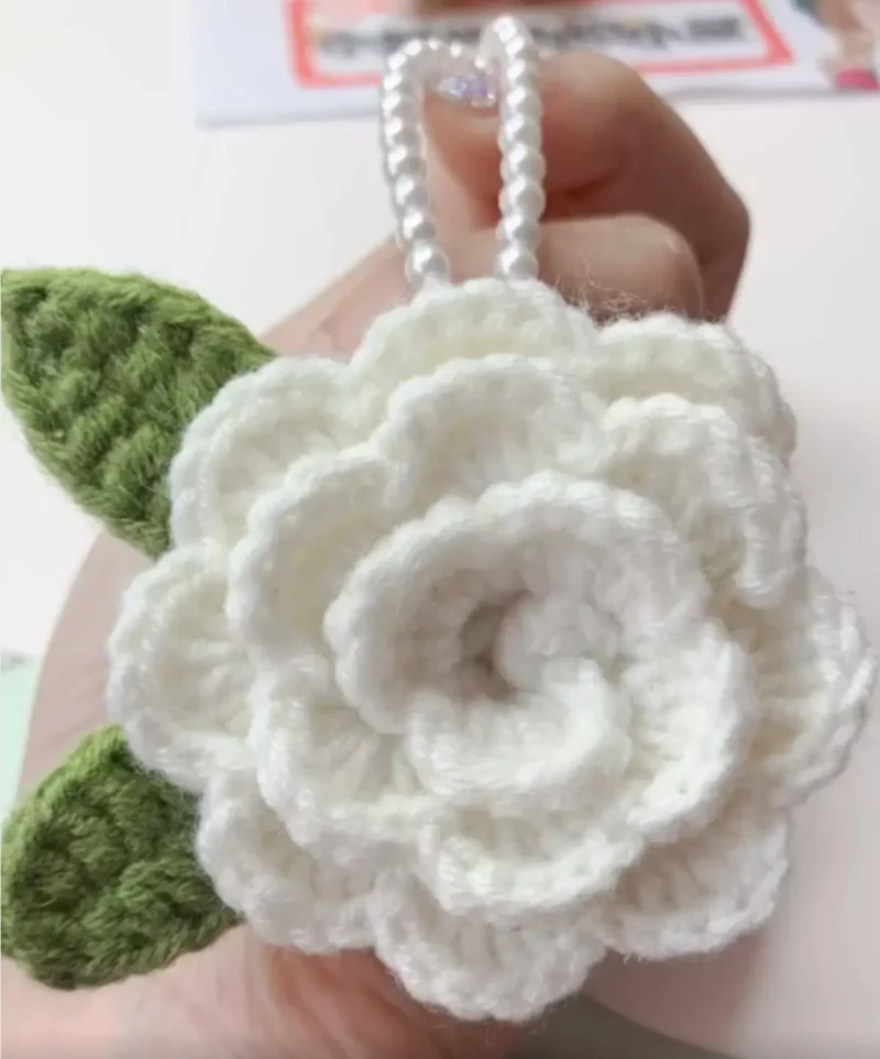 Crocheted white flower with green leaves, pearl necklace.