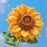 Crocheted sunflower with yellow petals and brown center, green leaves.