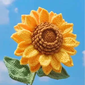 Crocheted sunflower with yellow petals and brown center, green leaves.