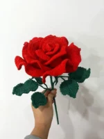 Crocheted red rose with green leaves.