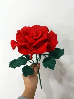 Crocheted red rose with green leaves.