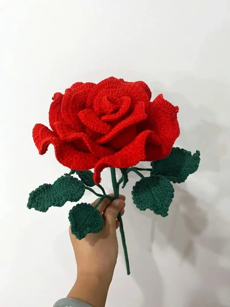 Crocheted red rose with green leaves.