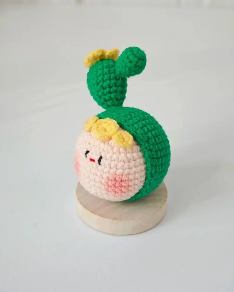 Crocheted cactus-themed doll,  pink face, green top.