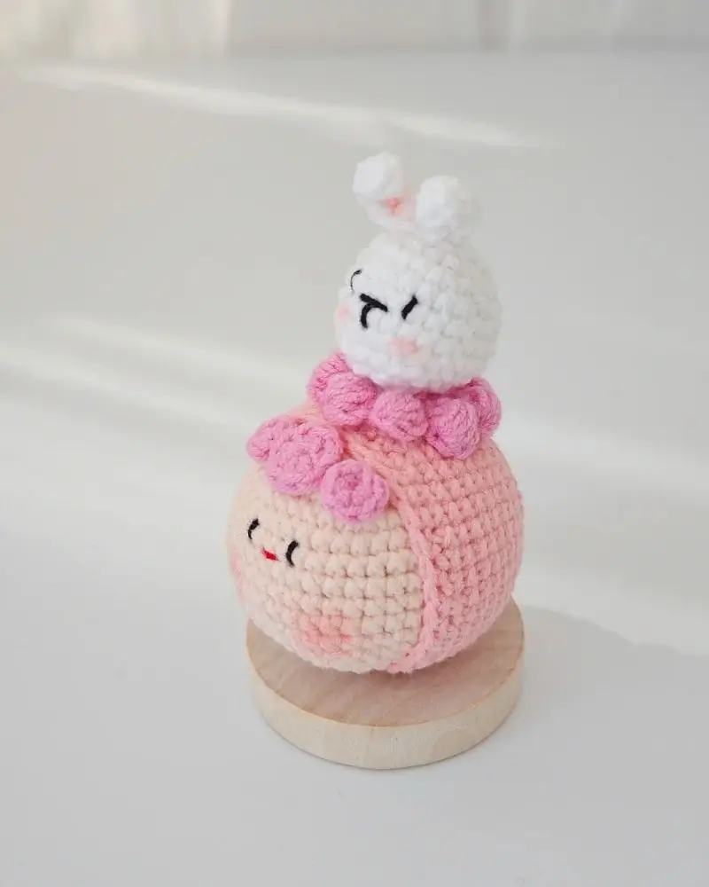 Cute crocheted bunny on a pink ball, wooden base.