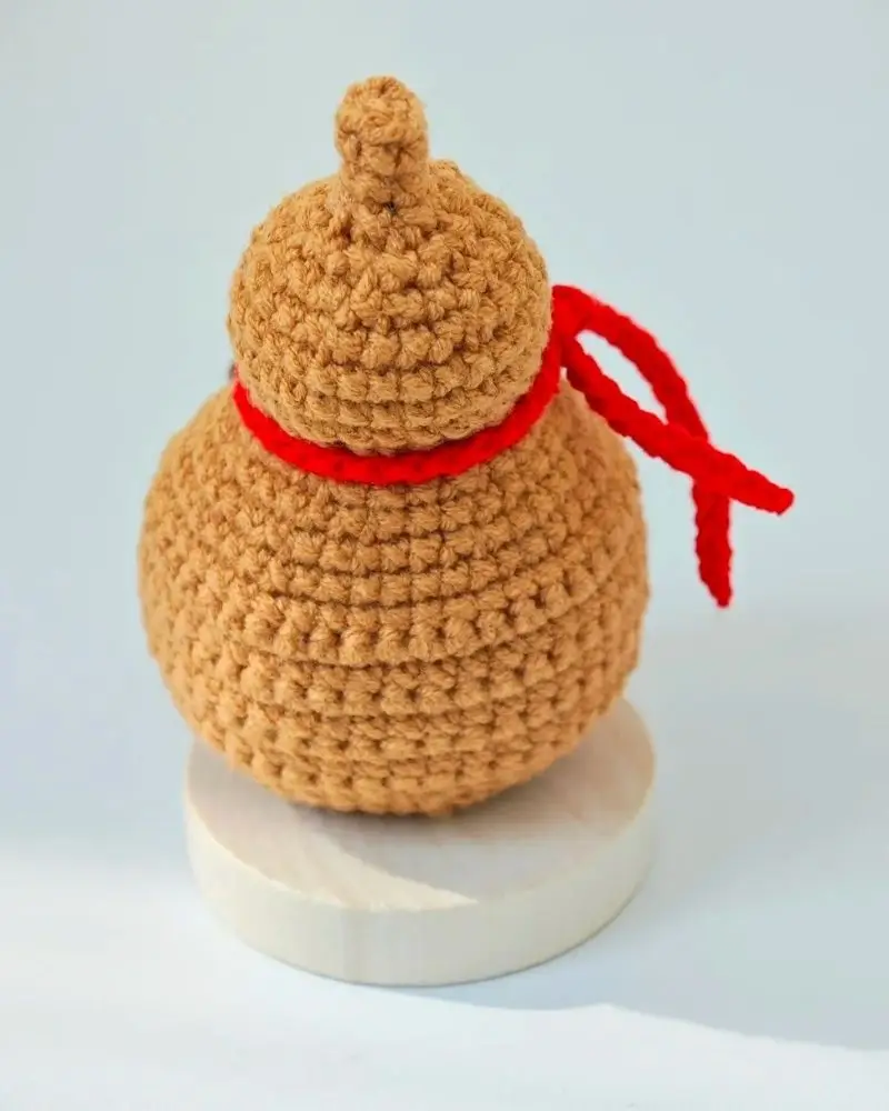 Crocheted mini gourd, tan color, red ribbon.