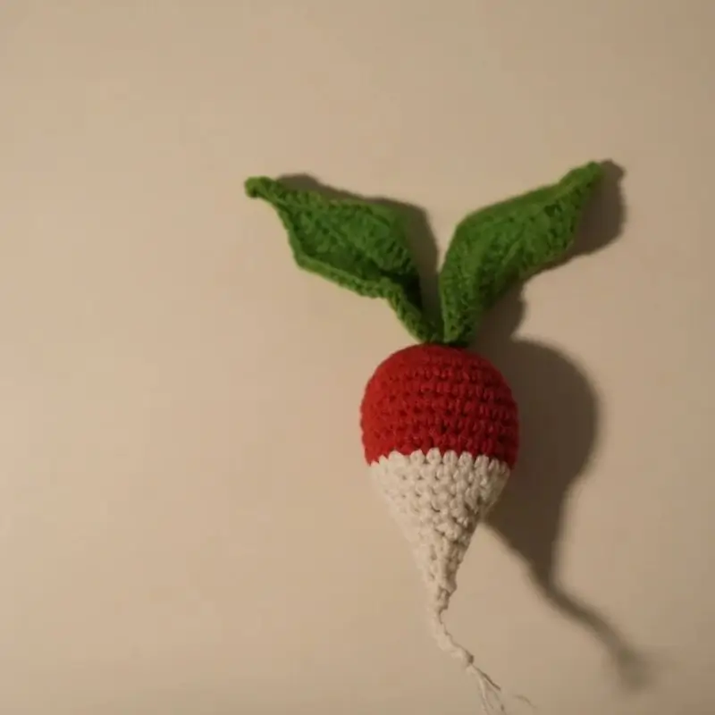 Crocheted radish toy, red and white, green leaves.