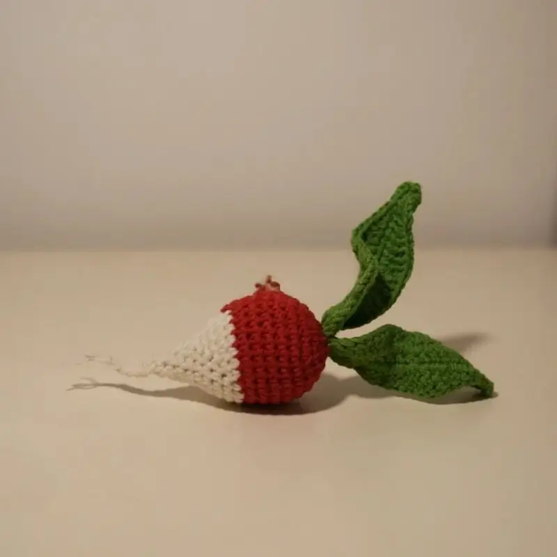 Crocheted radish toy, red and white, green leaves.