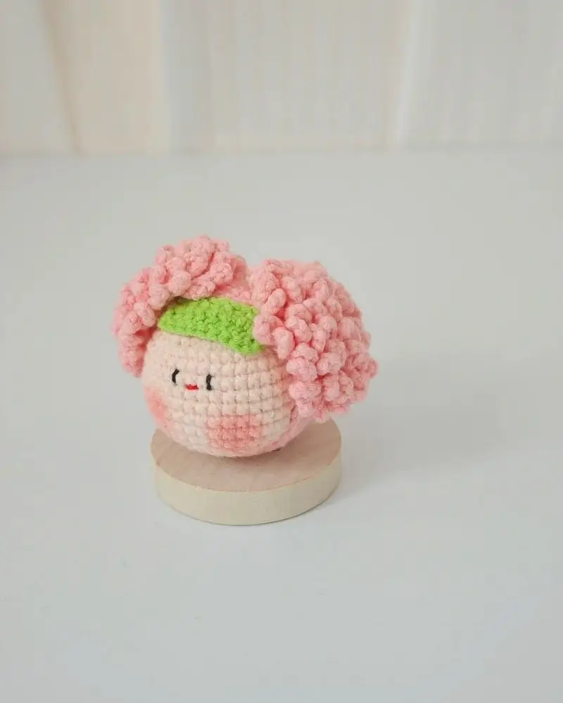 Pink crocheted doll, cute face, green headband.