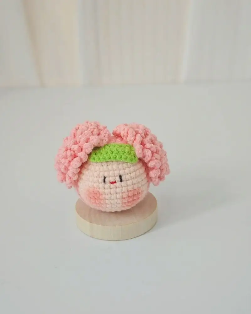 Pink crocheted doll, cute face, green headband.