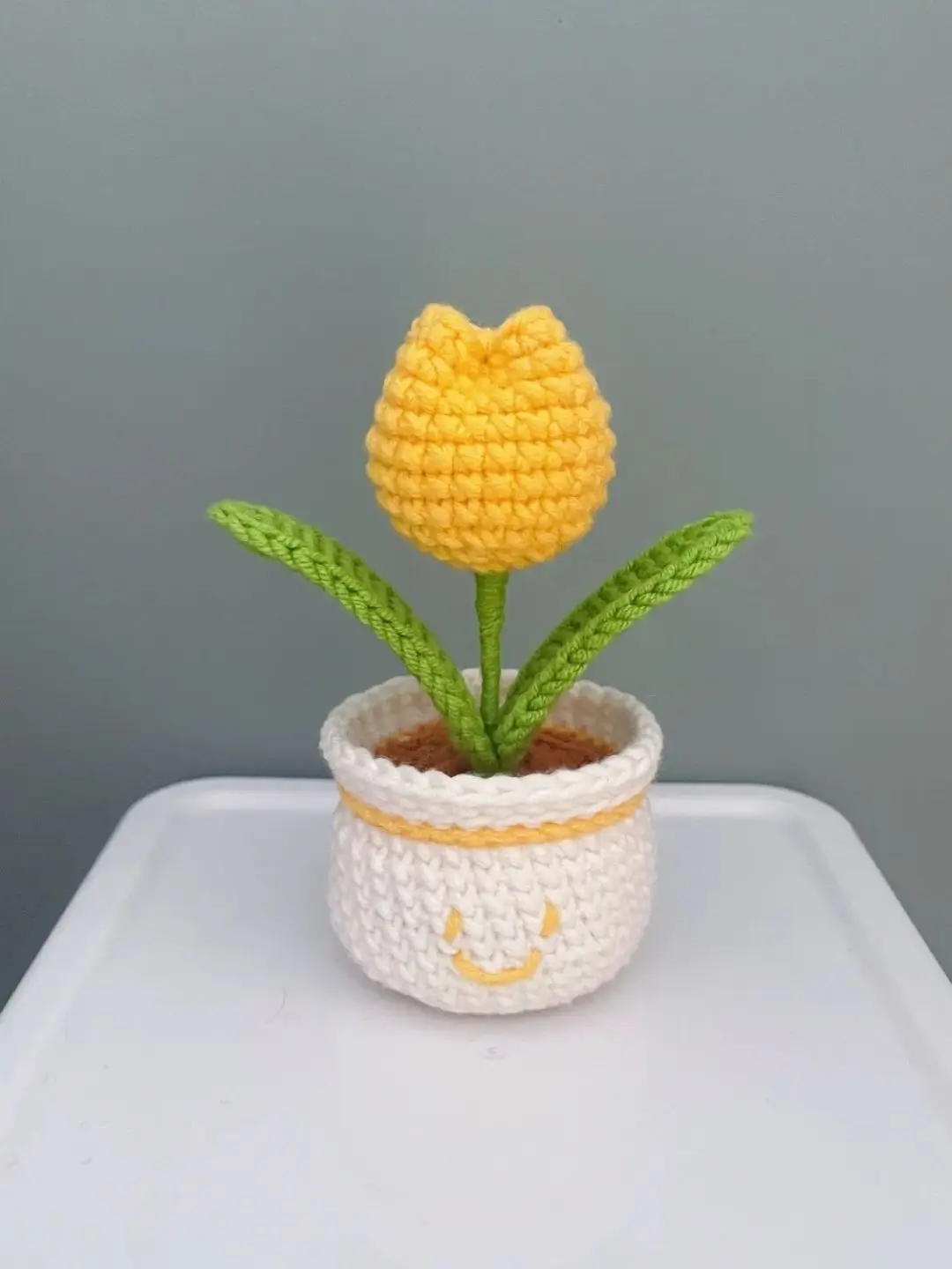 Crocheted yellow tulip in white pot with smiley face.