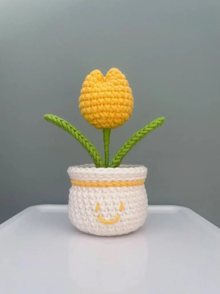 Crocheted yellow tulip in white pot with smiley face.