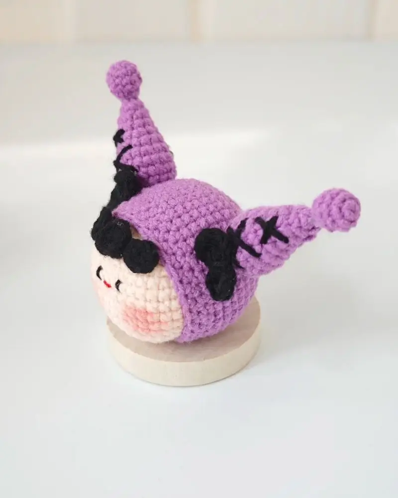 Purple crocheted character with pointy hat, black details.