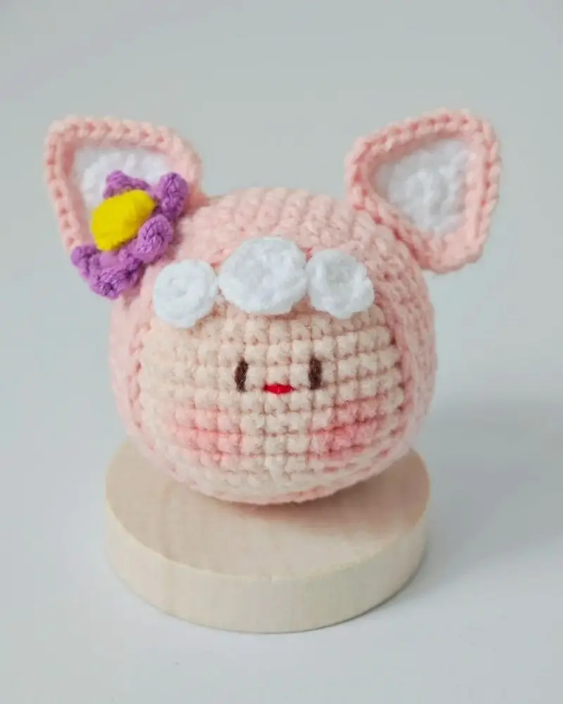 Pink crocheted lamb figurine with flower.