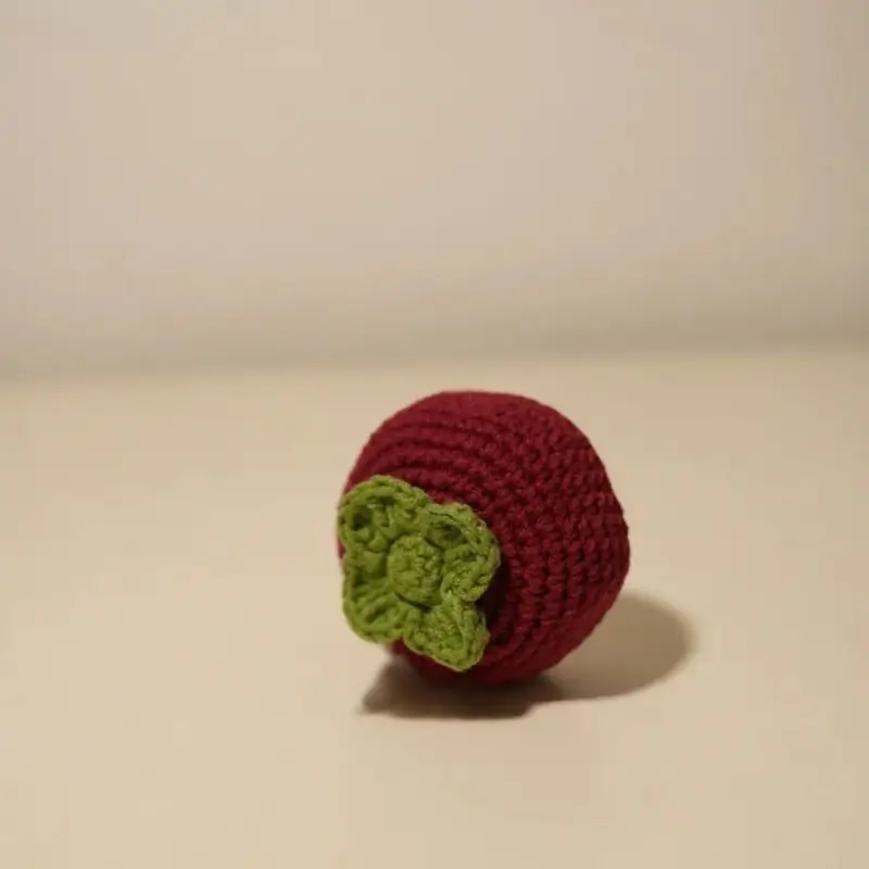 Crocheted maroon fruit, green leaf.