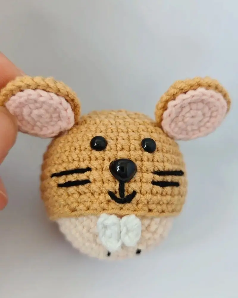 Crocheted mouse toy, light brown, pink ears, black eyes.