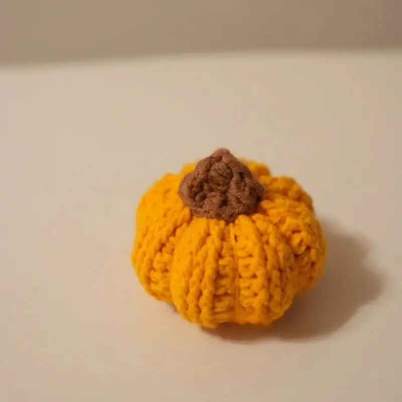 Small crocheted pumpkin, orange/yellow, brown stem.