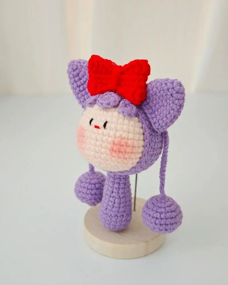 Cute purple crocheted doll with red bow.