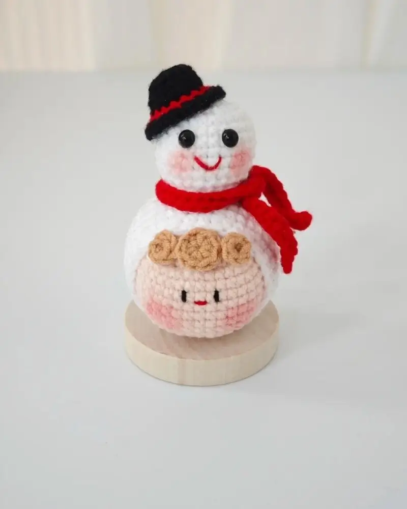 Crocheted snowman, red scarf, wooden base.