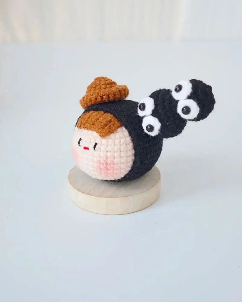 Crocheted doll, brown hat, black hair, big eyes.