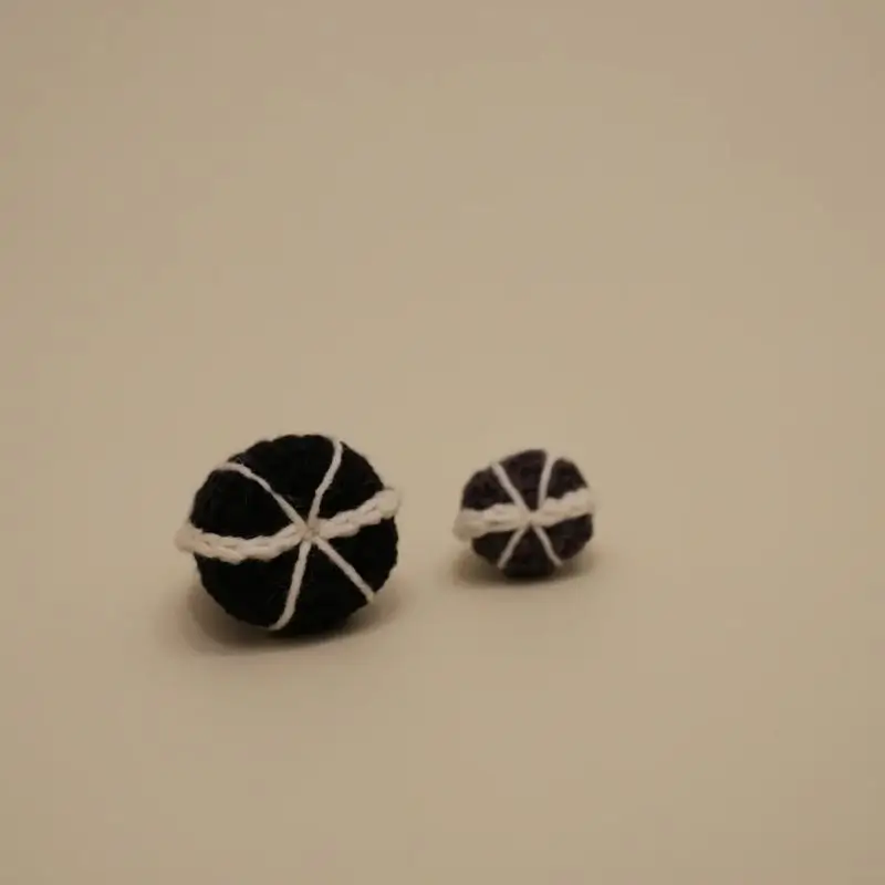 Two small crocheted dark balls with white stitching.