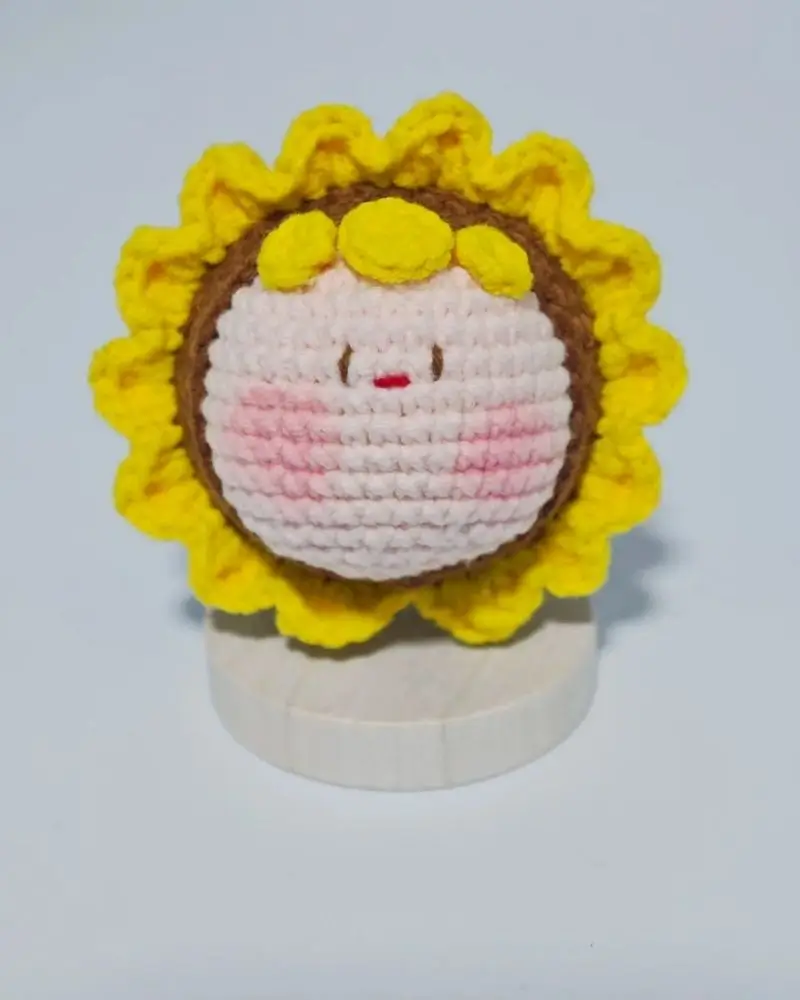 Crocheted sunflower face, yellow petals, pink center.