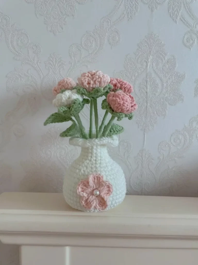 Crochet flower vase with pink and white flowers.