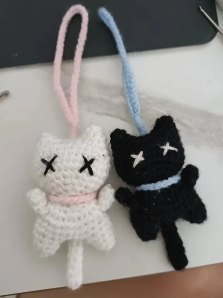 Two crocheted, dead-eyed cats, one white, one black.