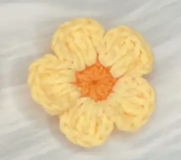 Crocheted yellow flower, orange center, close-up.