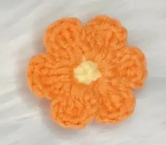 Orange crocheted flower, textured petals, yellow center.