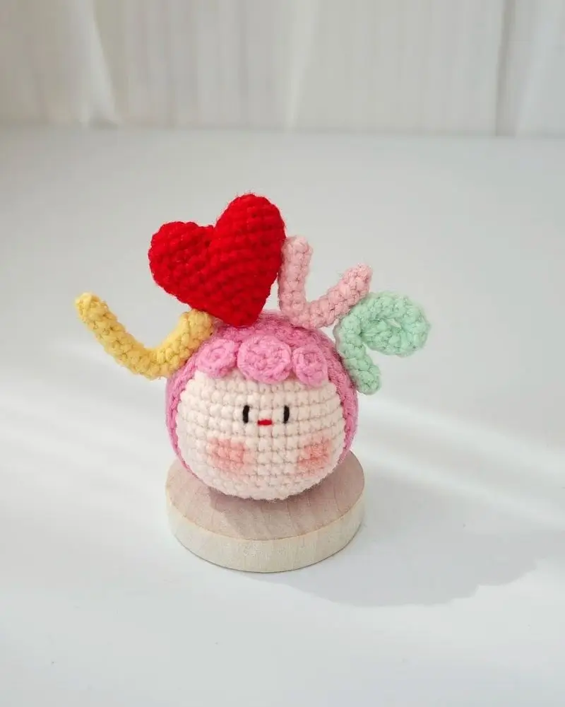 Crocheted pink character with red heart, pastel accents.  Cute little amigurumi.