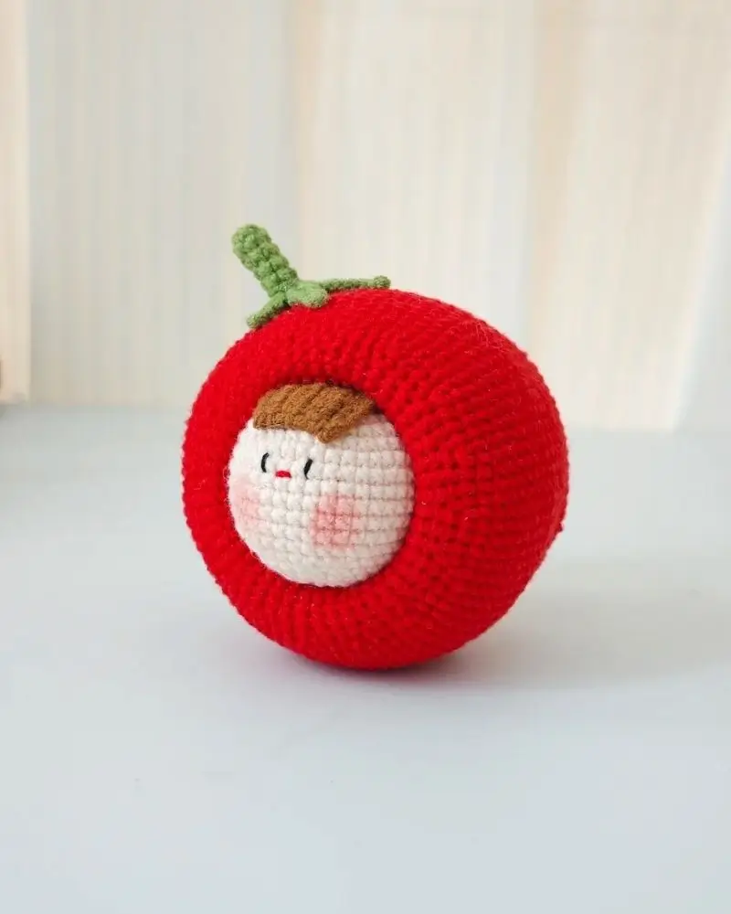Crocheted tomato-shaped toy with a face.