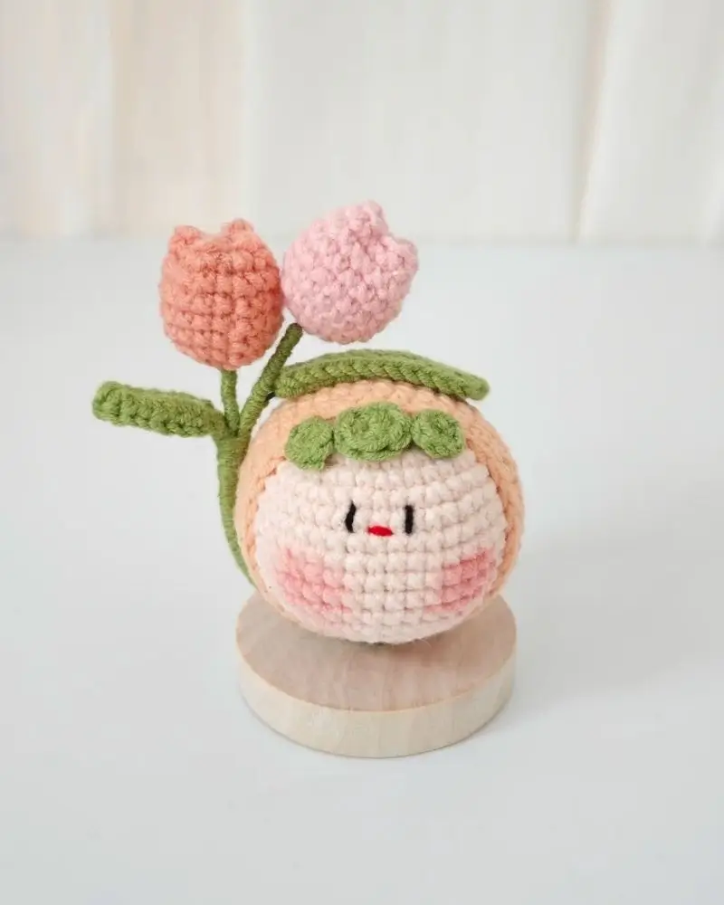 Cute crocheted doll with tulips, blush, and wooden base.