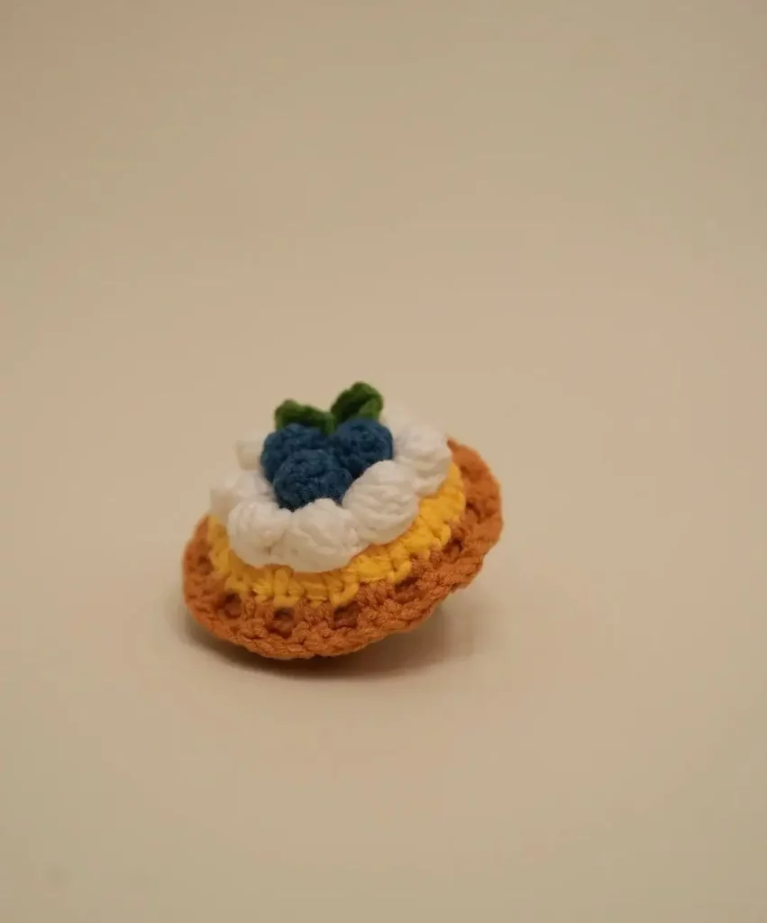 Crocheted blueberry tart, yellow and orange crust, white cream, blue blueberries.