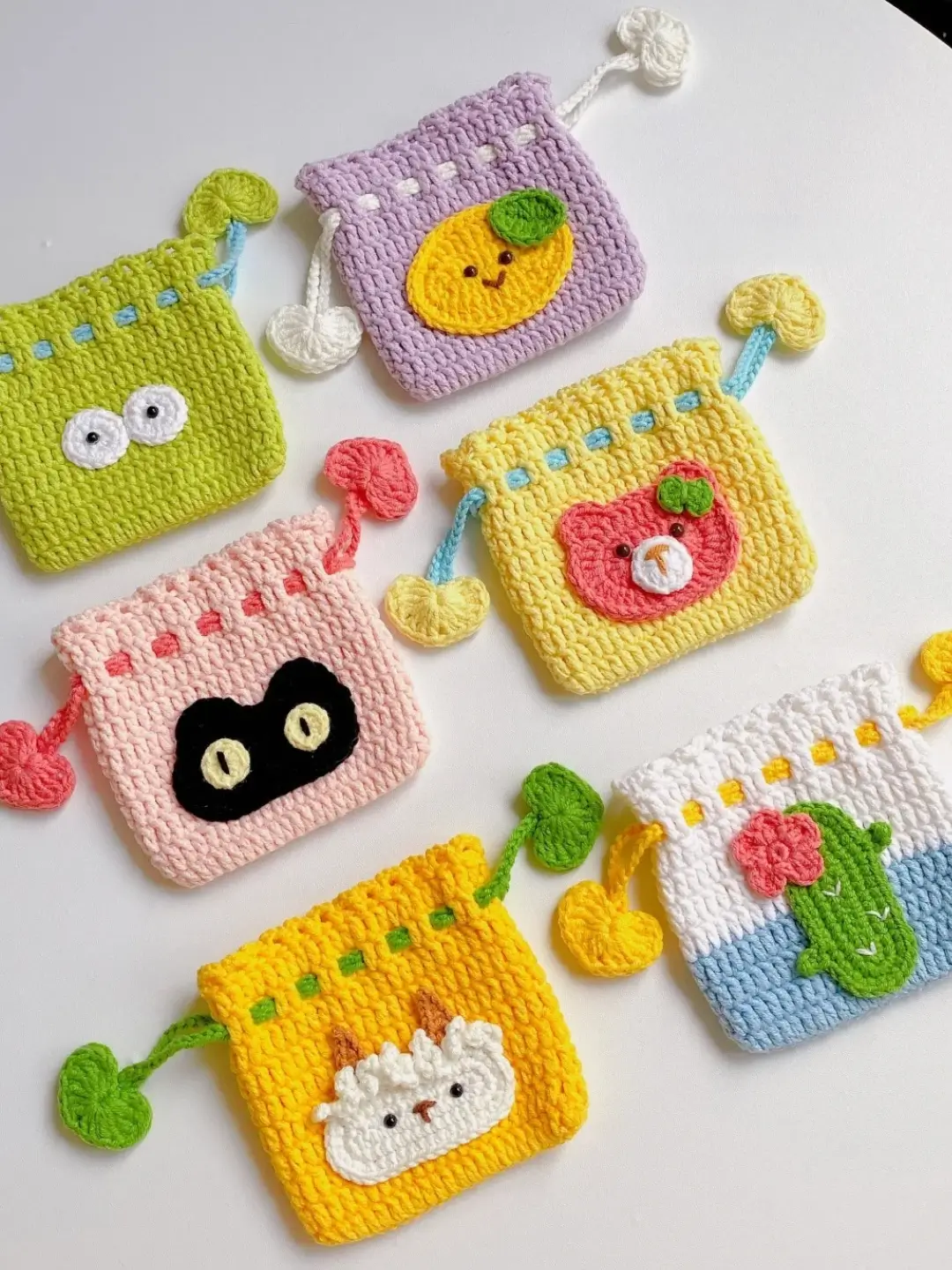 Colorful crocheted drawstring pouches, various animal and fruit designs.