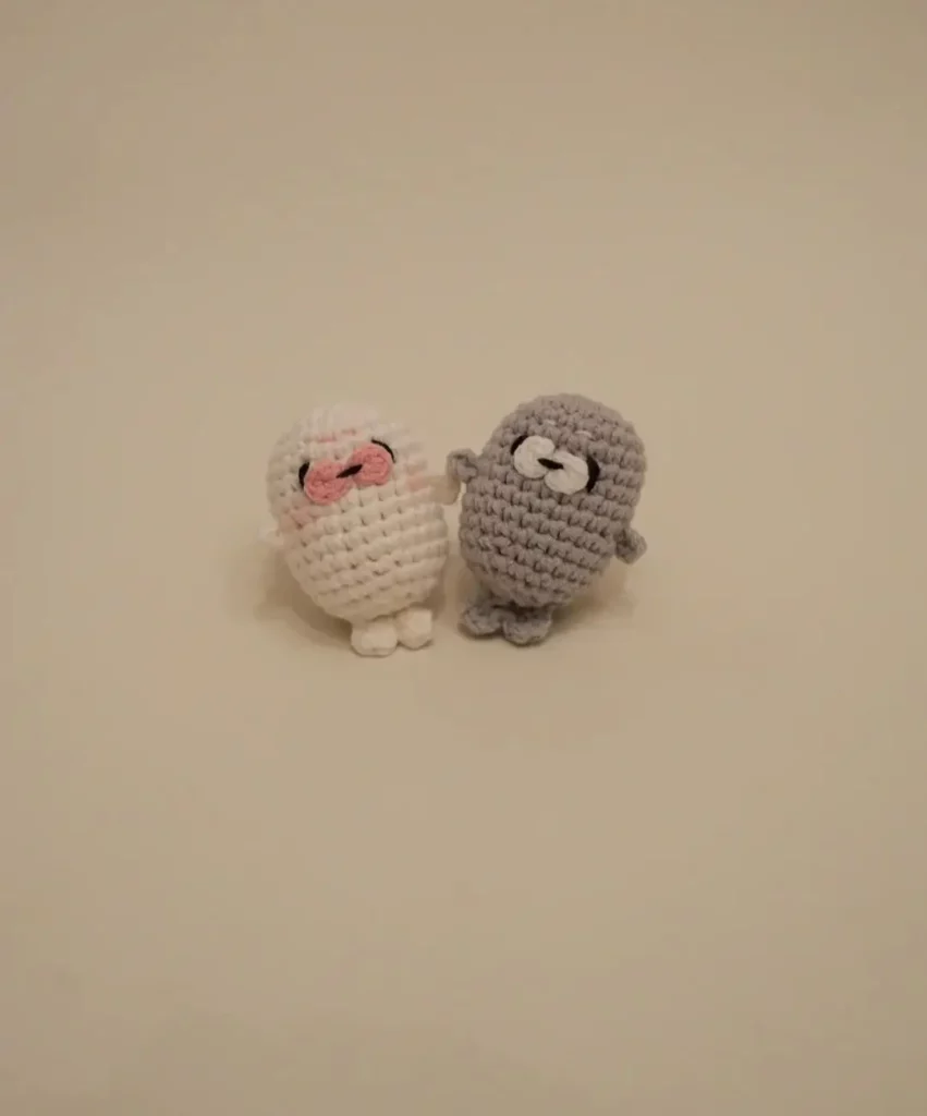 Two crocheted sea lion toys, one white, one gray.