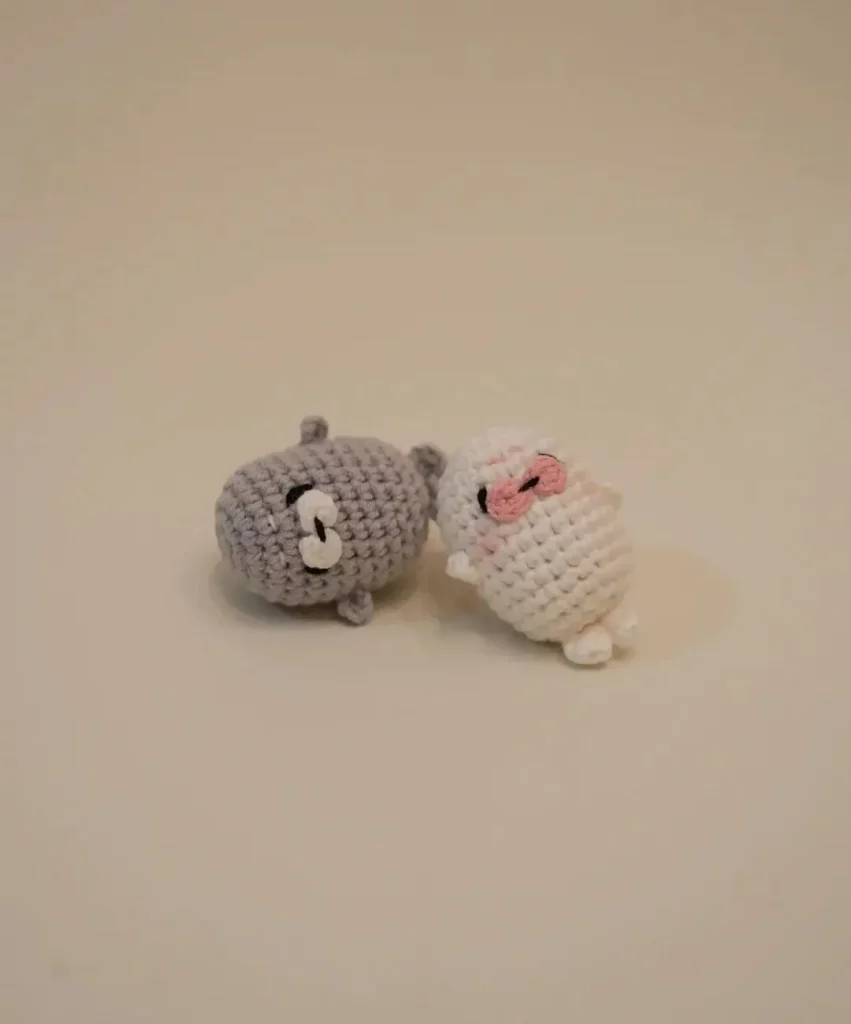 Two crocheted seal-like animals, gray and white, with pink accents.