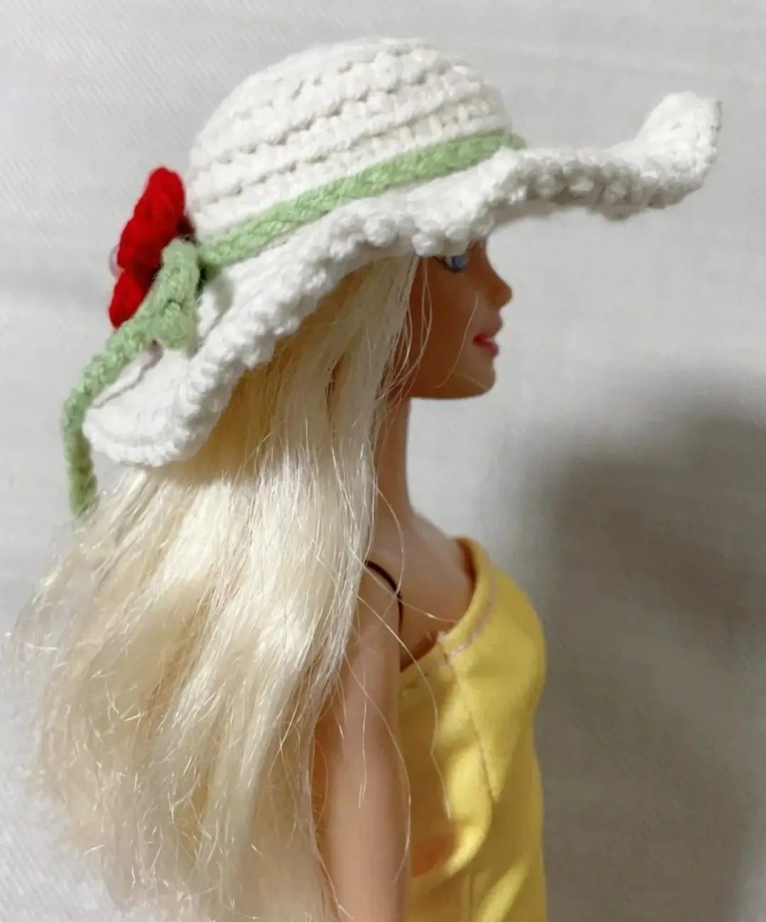 White crochet doll hat with green trim and red flower.