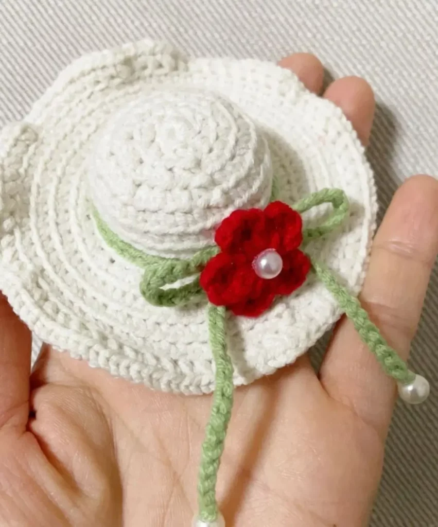 Crocheted white sun hat with red flower and green ribbon.