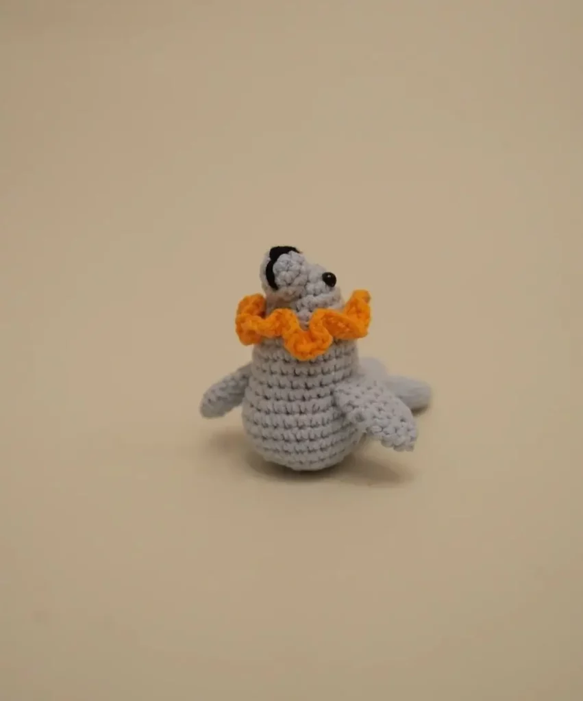 Crocheted light gray seal with orange ruffled collar.
