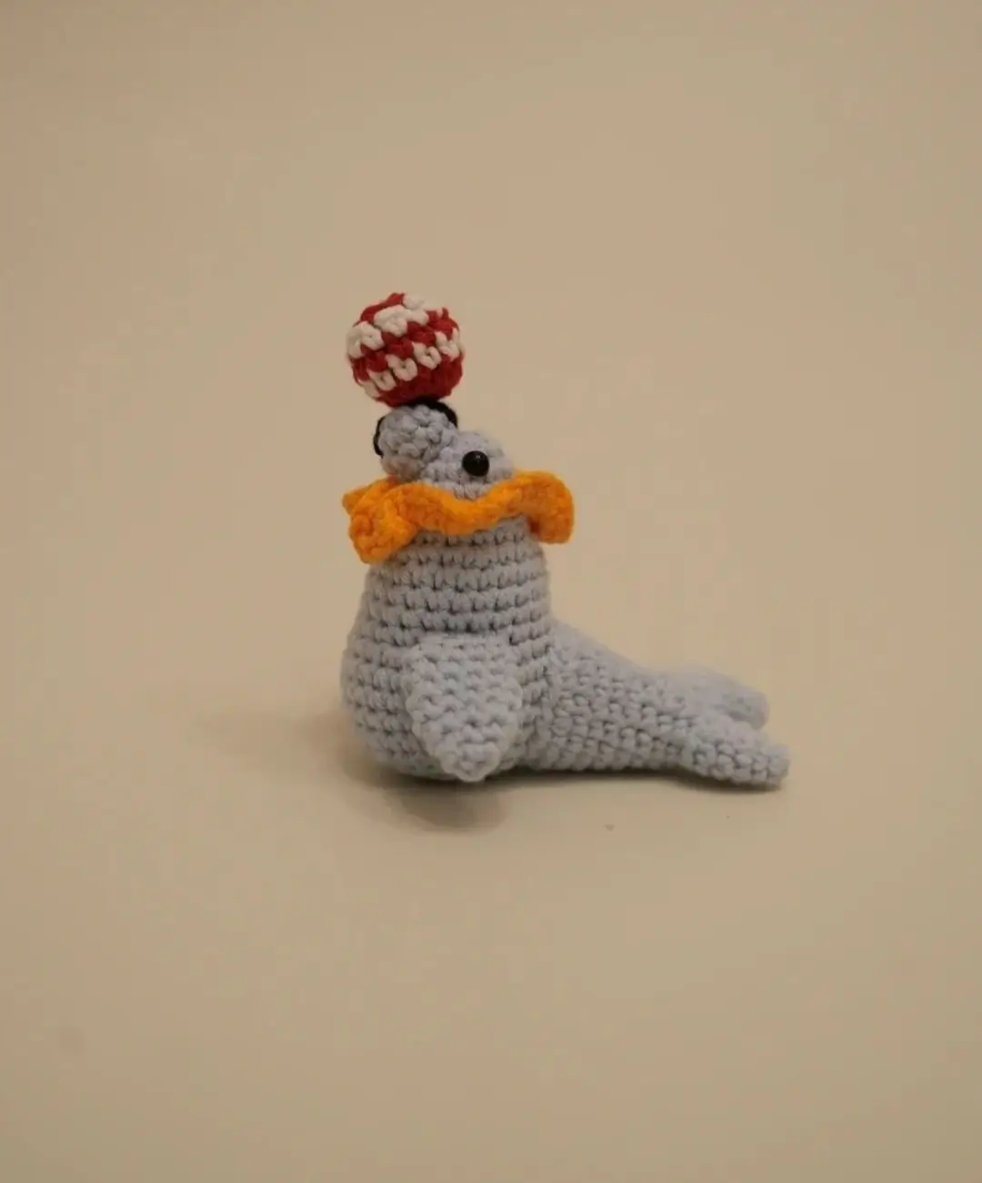 Crocheted light gray seal juggling red and white ball.