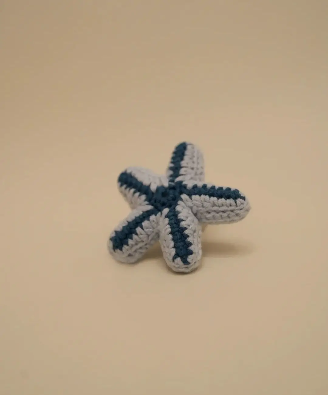 Crocheted starfish, light gray with navy blue stripes.