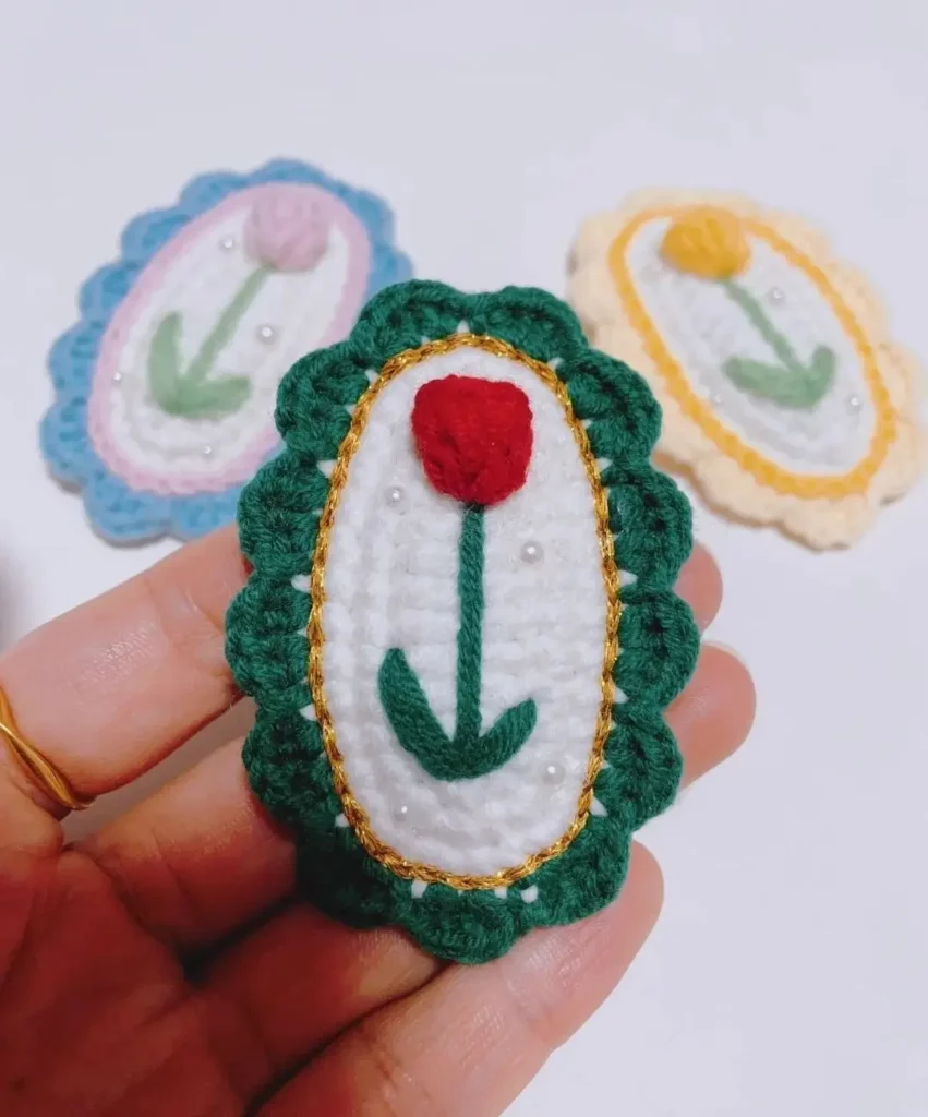 Crocheted oval brooch, red flower, white background, green trim.