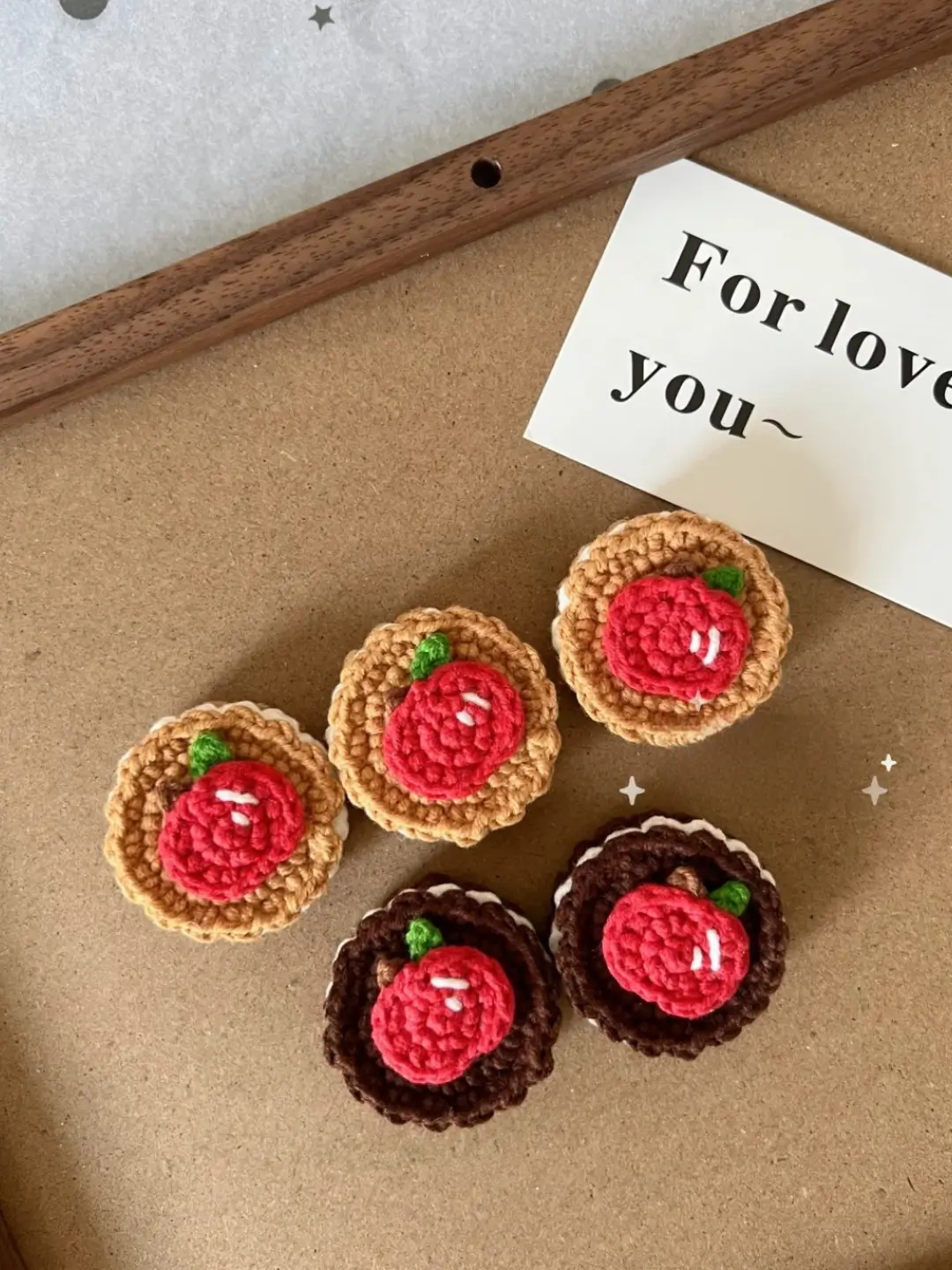 Crocheted apple cookies,  various colors,  on cork board.