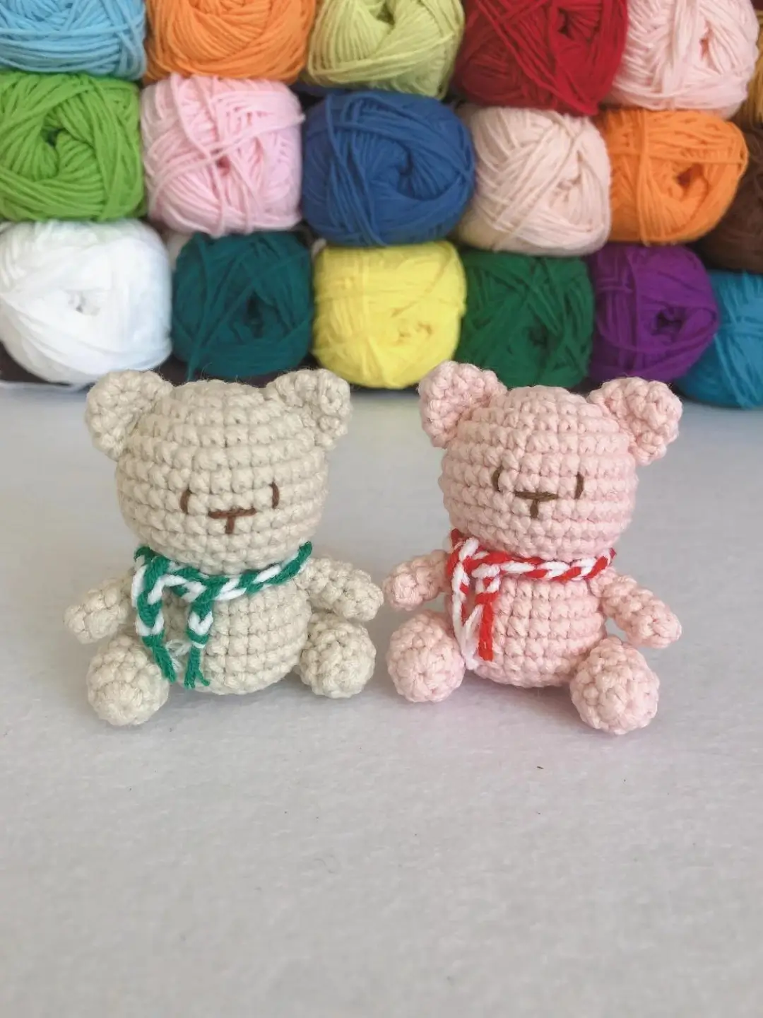 Two crocheted teddy bears, one beige, one pink, with green and red scarves.