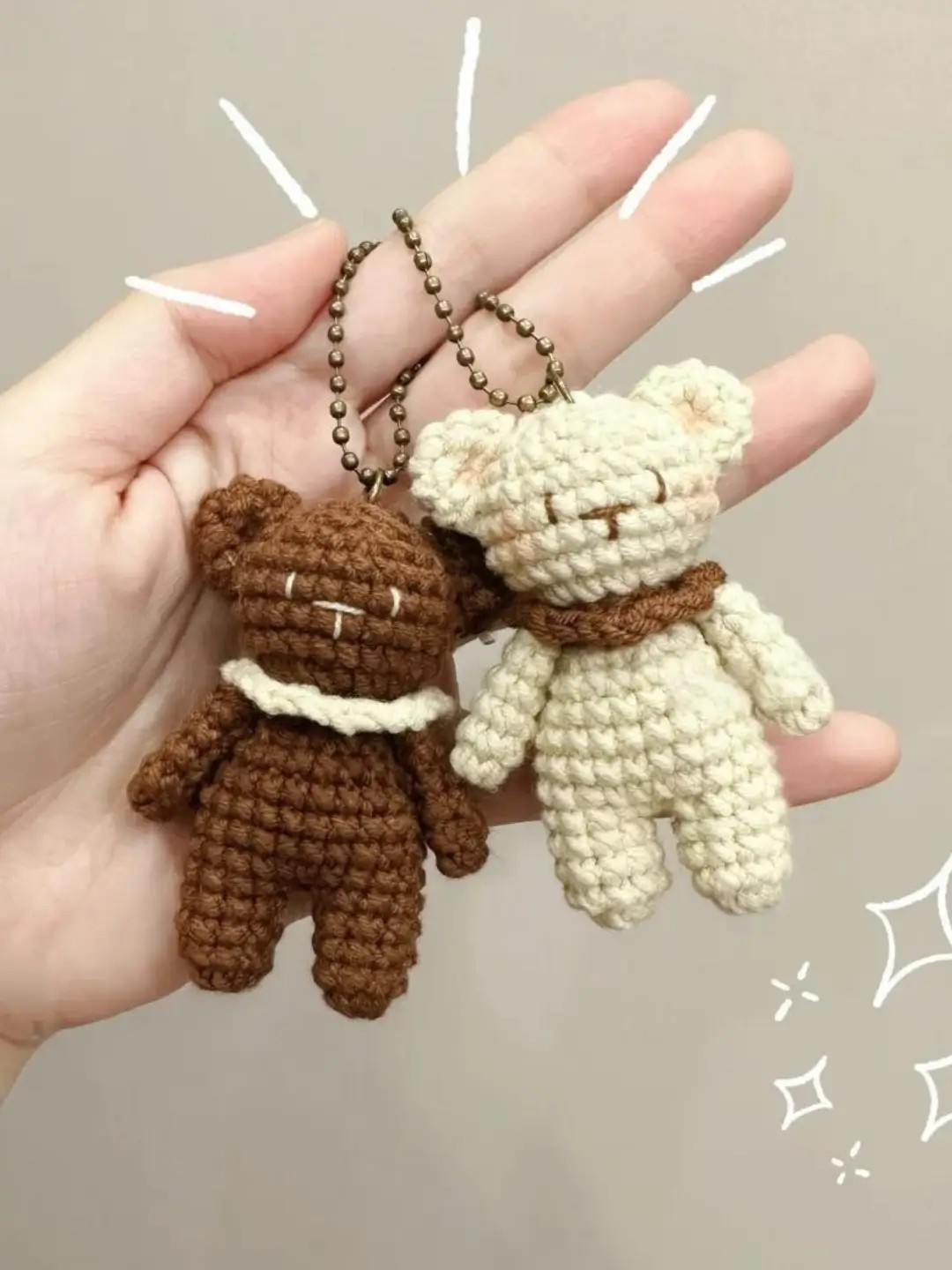 Two crocheted teddy bear keychains, brown and cream.