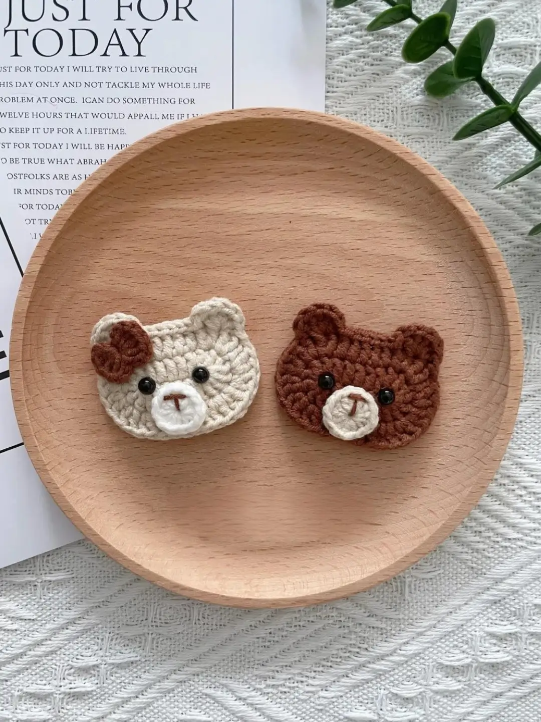 Crocheted bear faces, light beige and brown, on wooden plate.